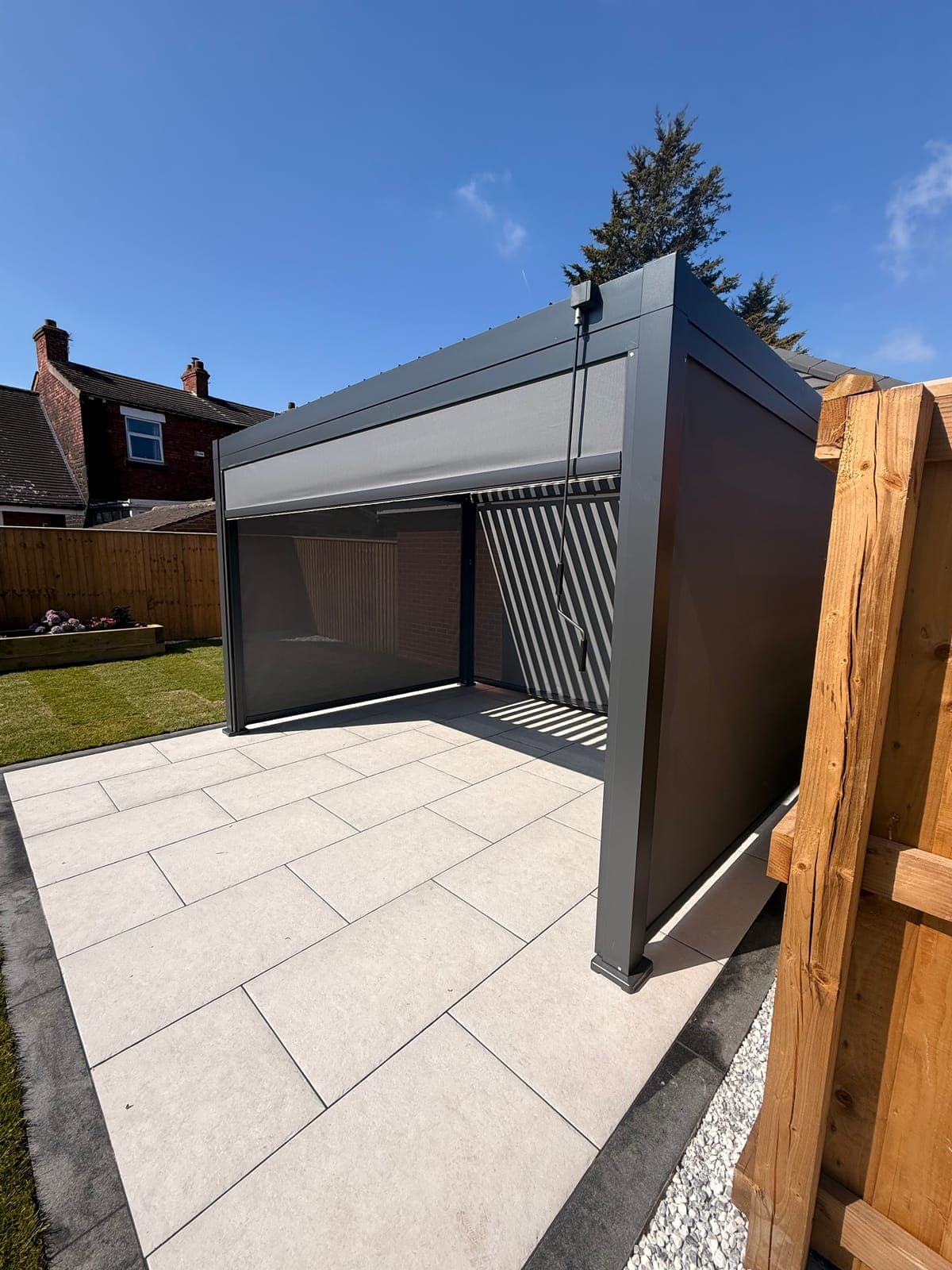 Garden Pergola — Aluminium louvered pergola with open roof slats beside a porcelain patio and lawn.